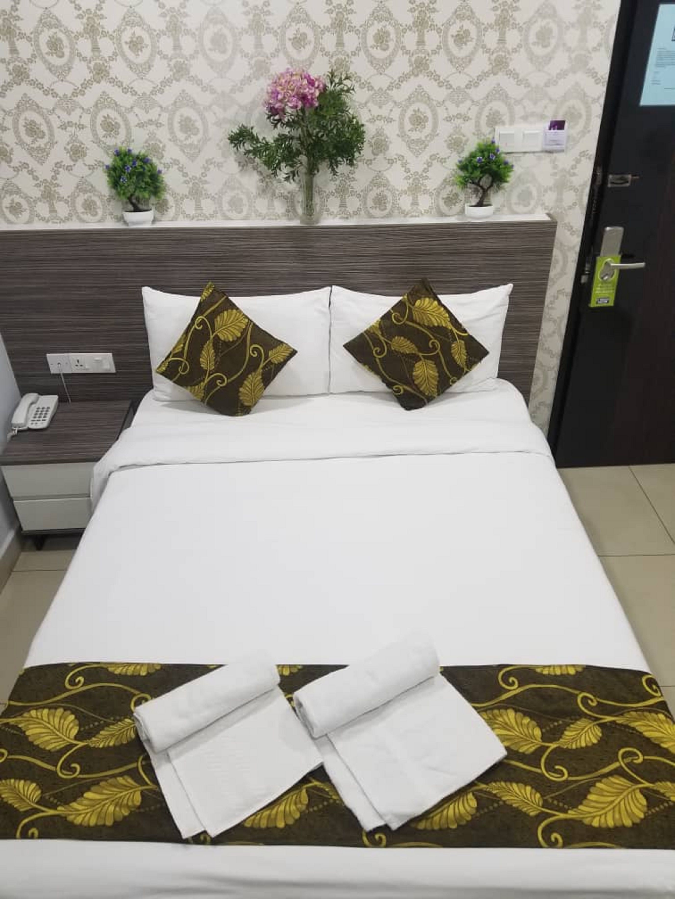 A neatly made bed with white linens and two decorative pillows with a leaf pattern. A folded white towel is placed on the bed.