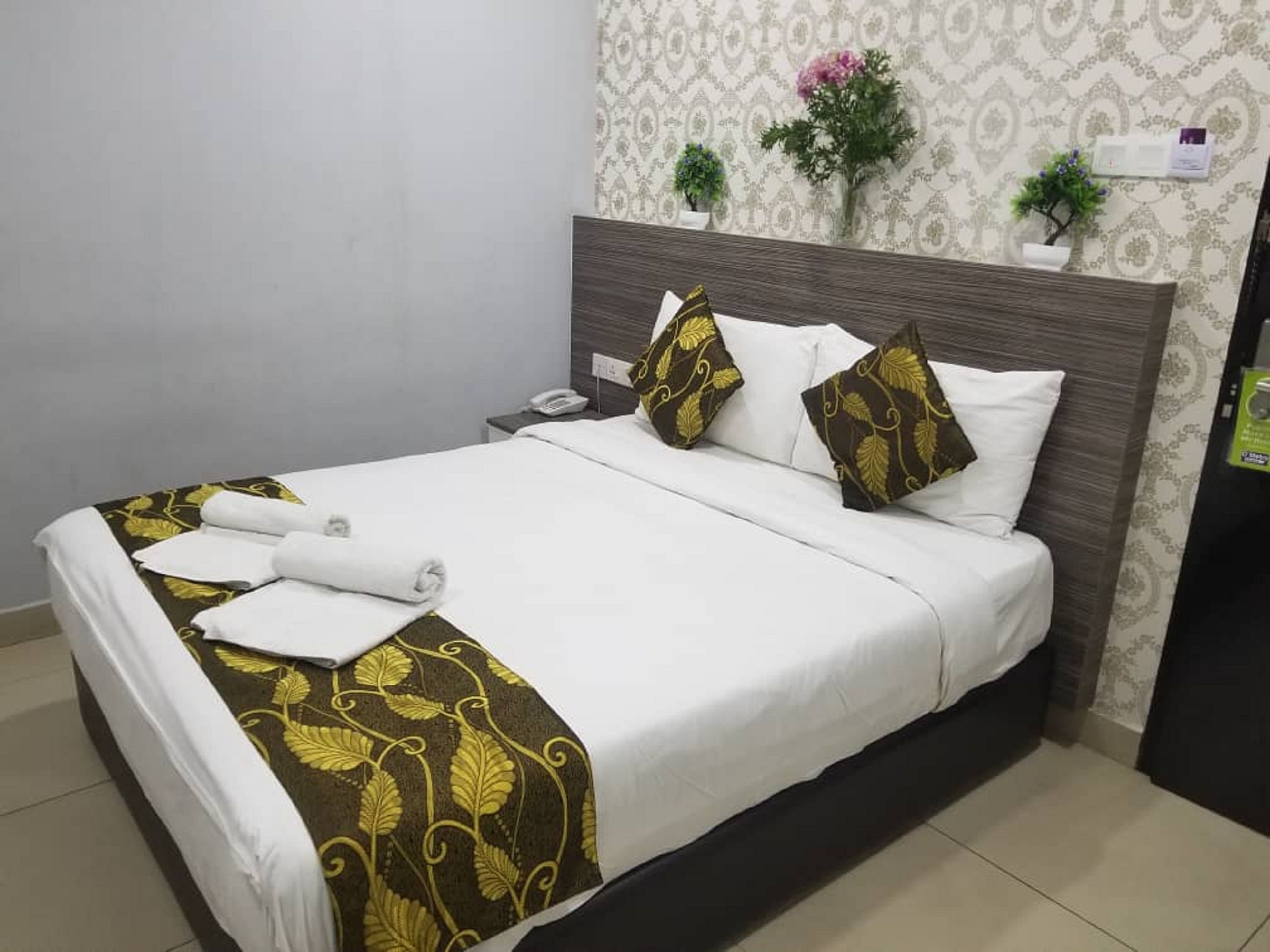 A neatly made bed with white and gold linens, a wooden headboard, and a bedside phone.