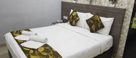 A neatly made bed with white and gold linens, a wooden headboard, and a bedside phone.
