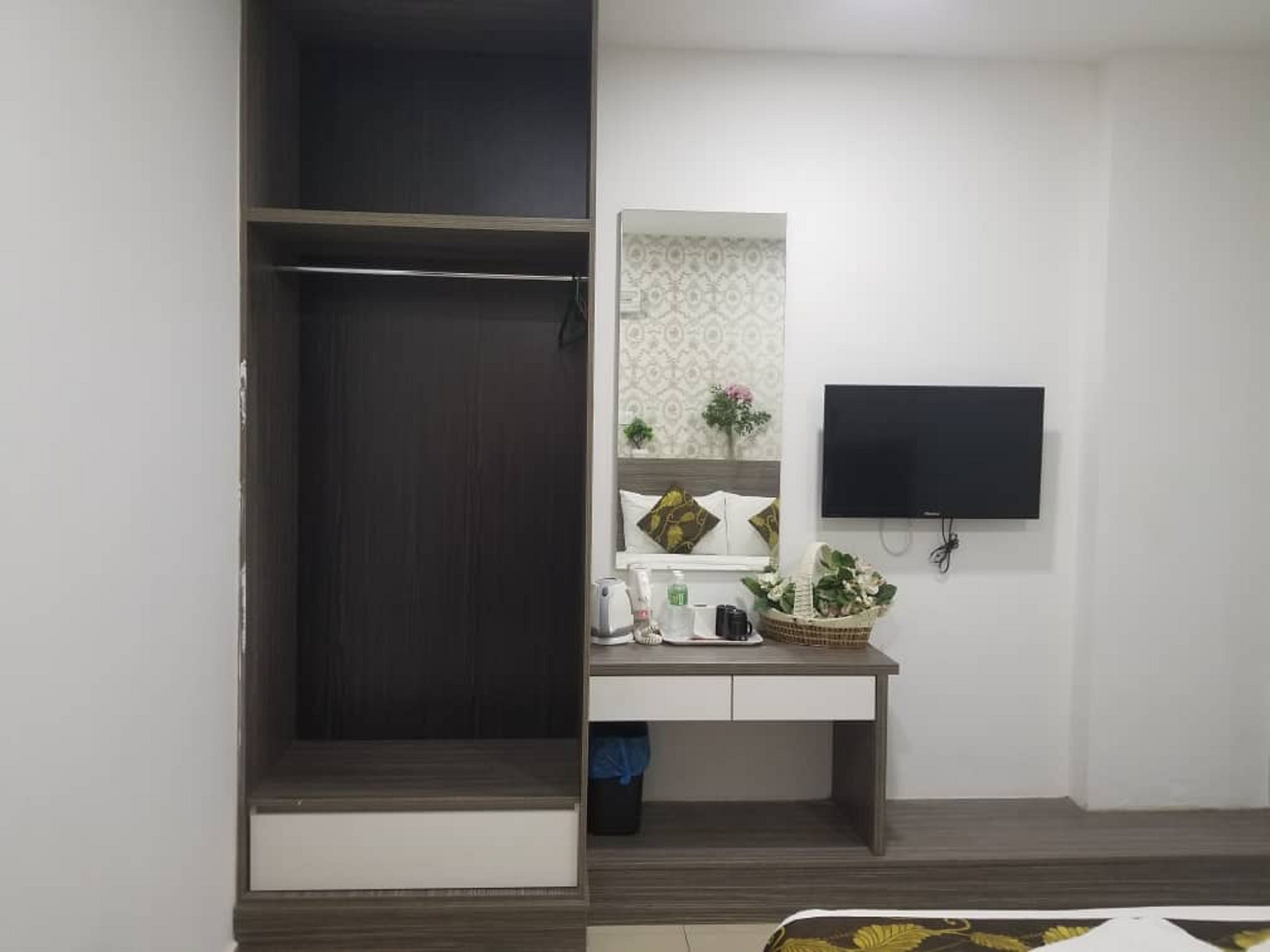 Une pièce avec une armoire en bois foncé, un petit bureau avec un miroir, un téléviseur à écran plat fixé au mur et une petite plante sur le bureau.