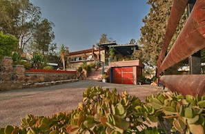 A building with a red garage door, a staircase leading to a covered porch, and a stone wall with plants. - Desert View (Arad)