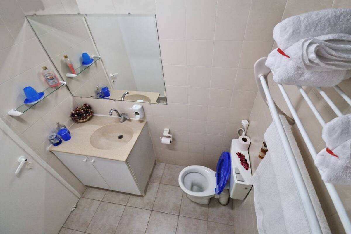 Un baño con lavamanos, espejo, inodoro y toallero.
