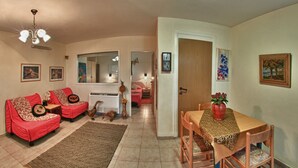 Een woonkamer met een rode bank, een eettafel met stoelen, een gekleurd tapijt en een plafondventilator.
