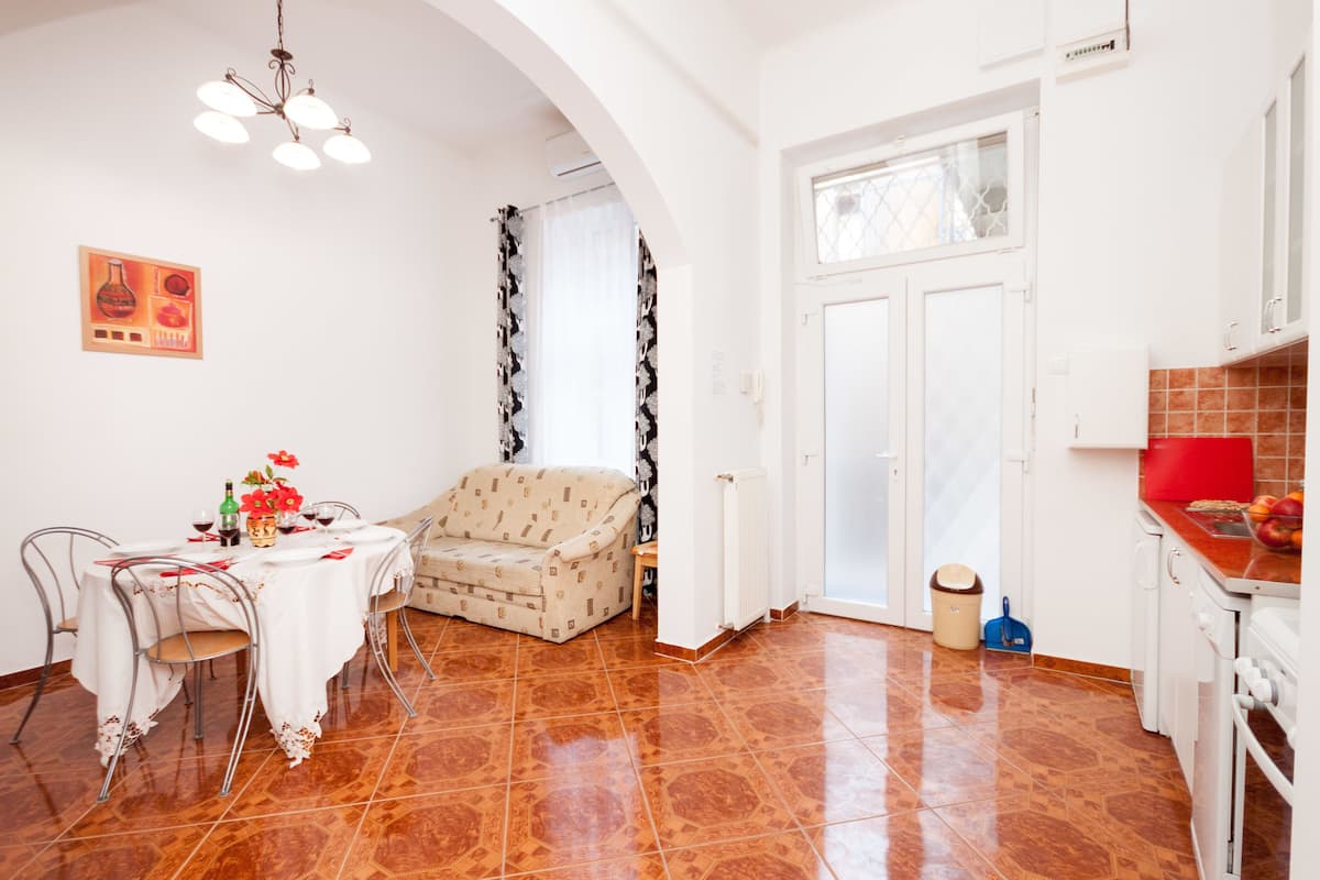 A dining area with a table set for two, a sofa, and a kitchen area with a stove and countertop.