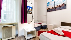 Habitación de hotel con cama, escritorio, silla, ventana con cortinas, calefactor, espejo y un cuadro en la pared.