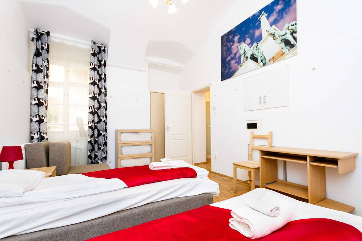A hotel room with two beds, a desk, a chair, and a painting on the wall.