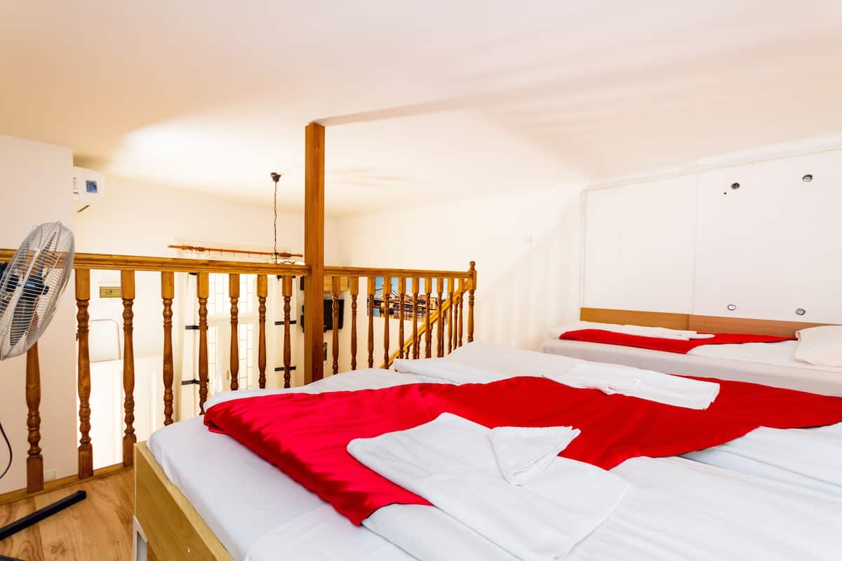 A hotel room with two beds, a wooden headboard, a standing fan, and a white wardrobe.
