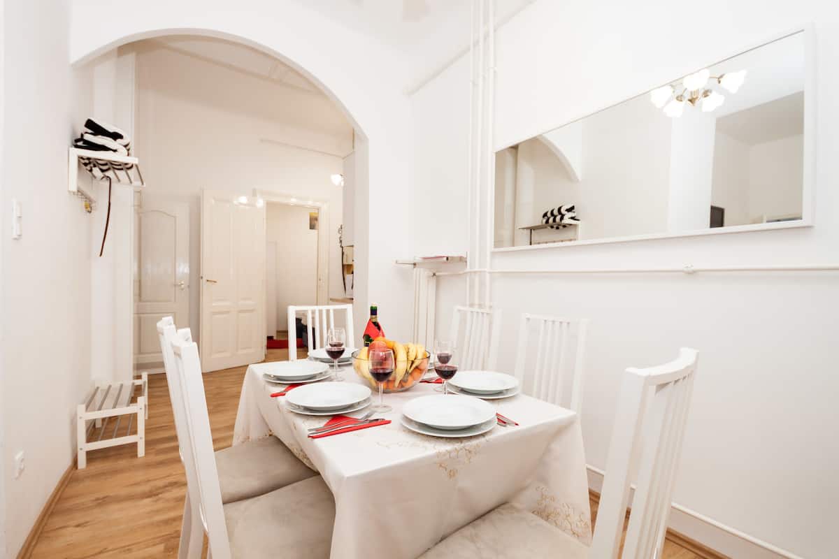 A dining area with a table set for four, white chairs, a mirror on the wall, and a small white stool.