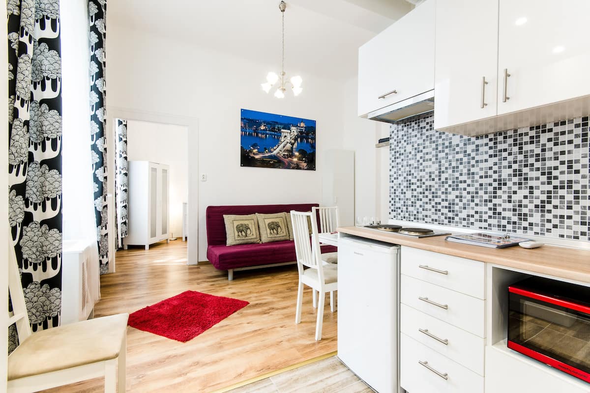 A modern kitchen with white cabinets, a red oven, and a dining area with a red rug.