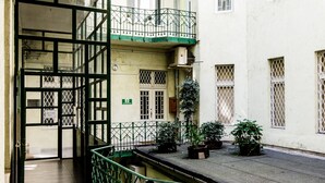 Un callejón estrecho con una barandilla de metal verde, una puerta con un letrero y un edificio con varias ventanas y balcones.