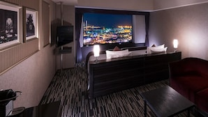 Une chambre d’hôtel avec un grand écran de télévision diffusant une vue sur la ville, un lit, un canapé rouge et une petite table avec une lampe.