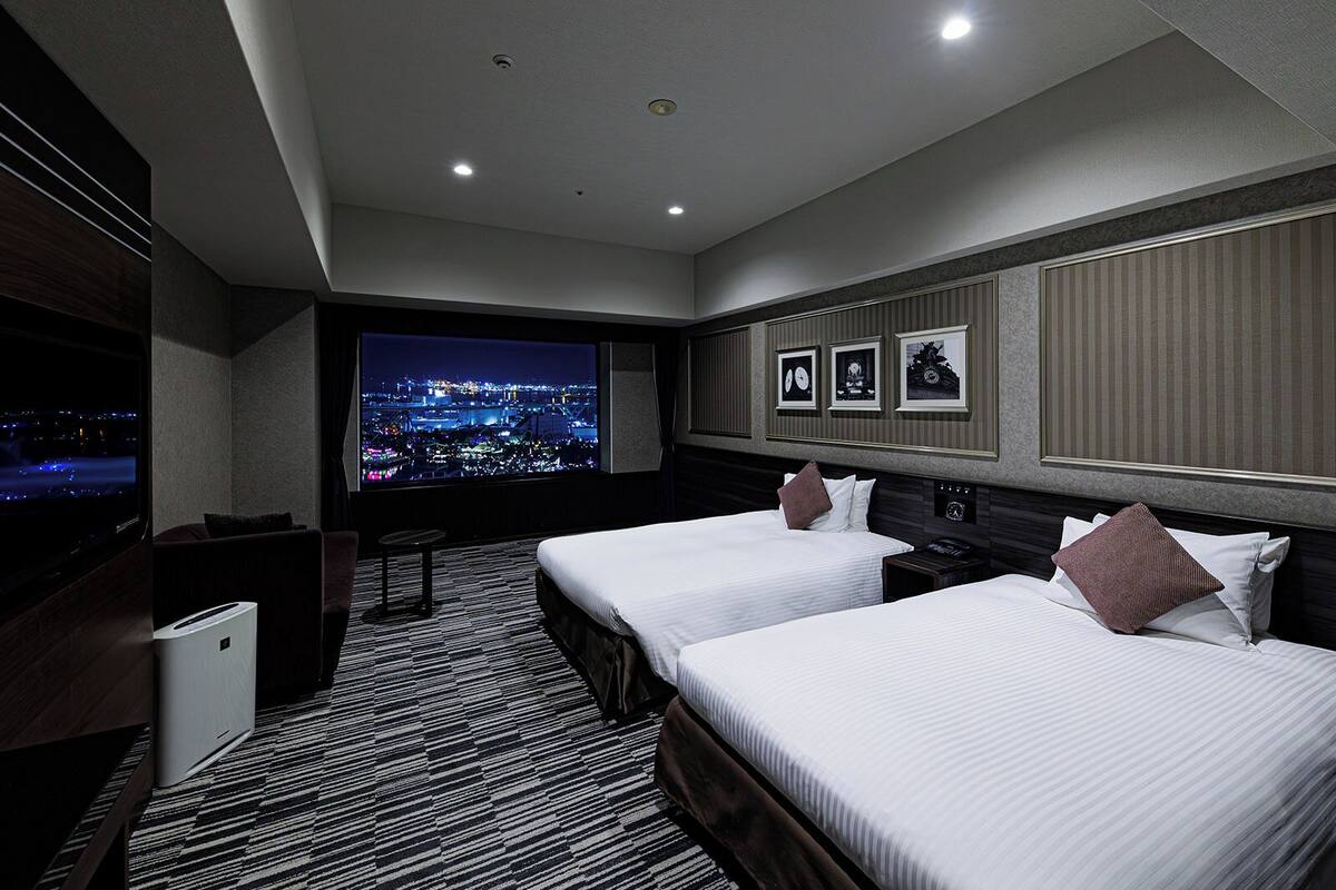 Quarto de hotel com duas camas, uma televisão grande, vista para a cidade e minibar.