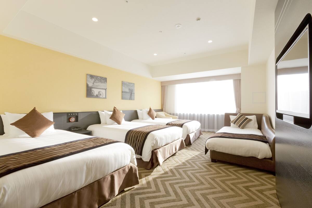 Een hotelkamer met drie bedden, een groot raam en een flatscreen televisie.