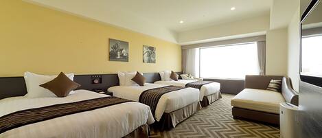 A hotel room with three beds, a sofa, and a large window providing natural light.