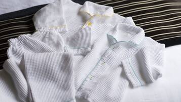 A neatly folded white garment with green trim on a bed with striped pillows.