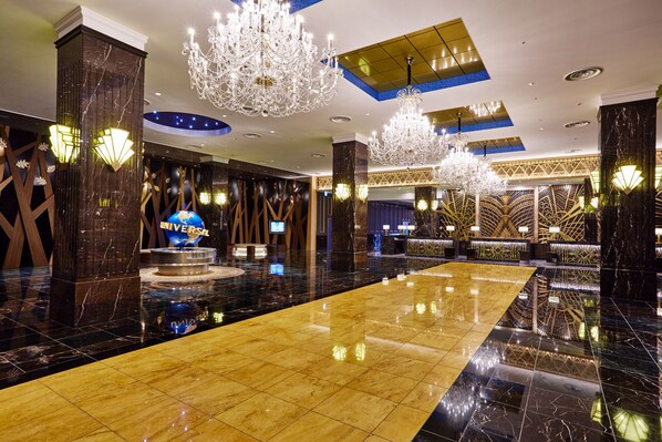 A spacious lobby with a polished marble floor, large chandeliers, and a prominent Universal logo.
