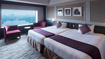 Una habitación de hotel con dos camas, un escritorio, una silla y vistas a la ciudad.