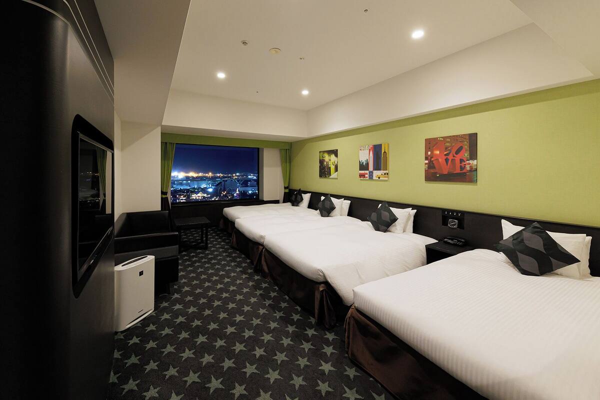 Quarto de hotel com duas camas, televisão, escrivaninha e janela com vista para a cidade.