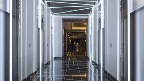 Un couloir d’hôtel moderne avec des carreaux noirs réfléchissants, des portes en verre et un luminaire central.