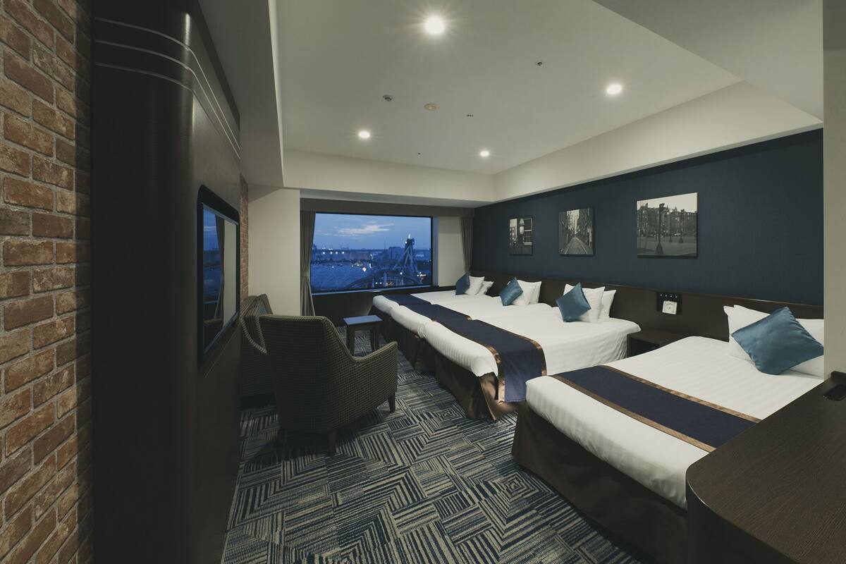 Quarto de hotel com duas camas, vista para a paisagem urbana, parede de tijolos e uma janela grande.