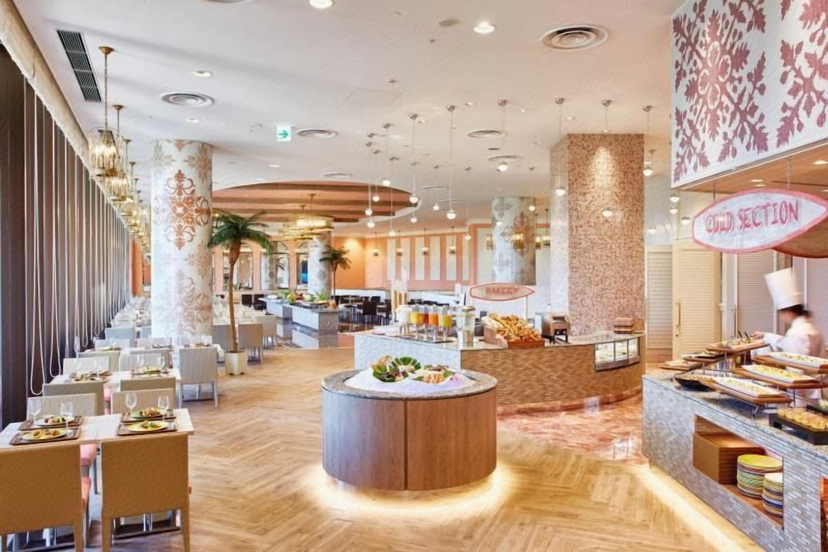 Um saguão de hotel com uma mesa redonda central, áreas de estar e um balcão de pastelaria.