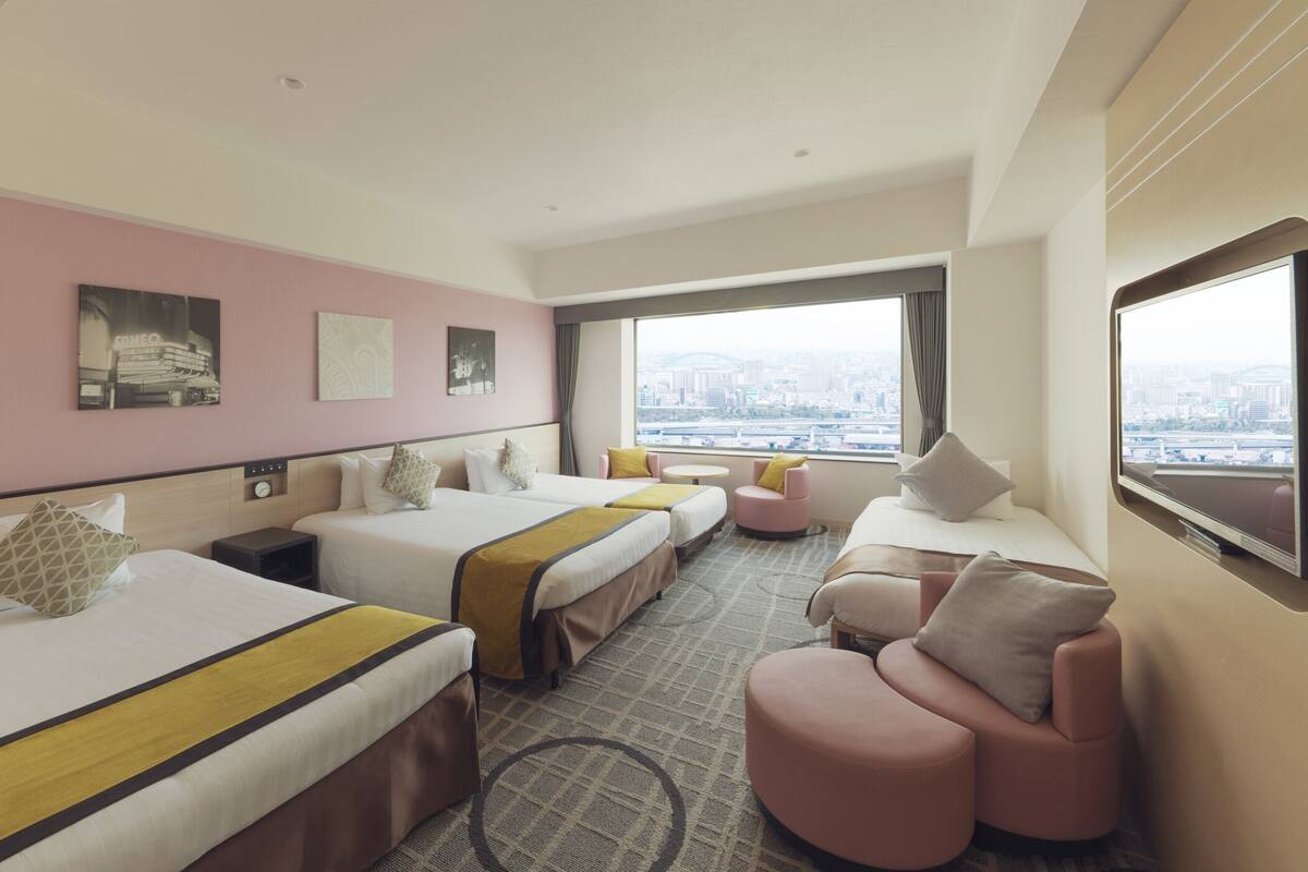 Een hotelkamer met twee bedden, een bank, een televisie en uitzicht over de stad.