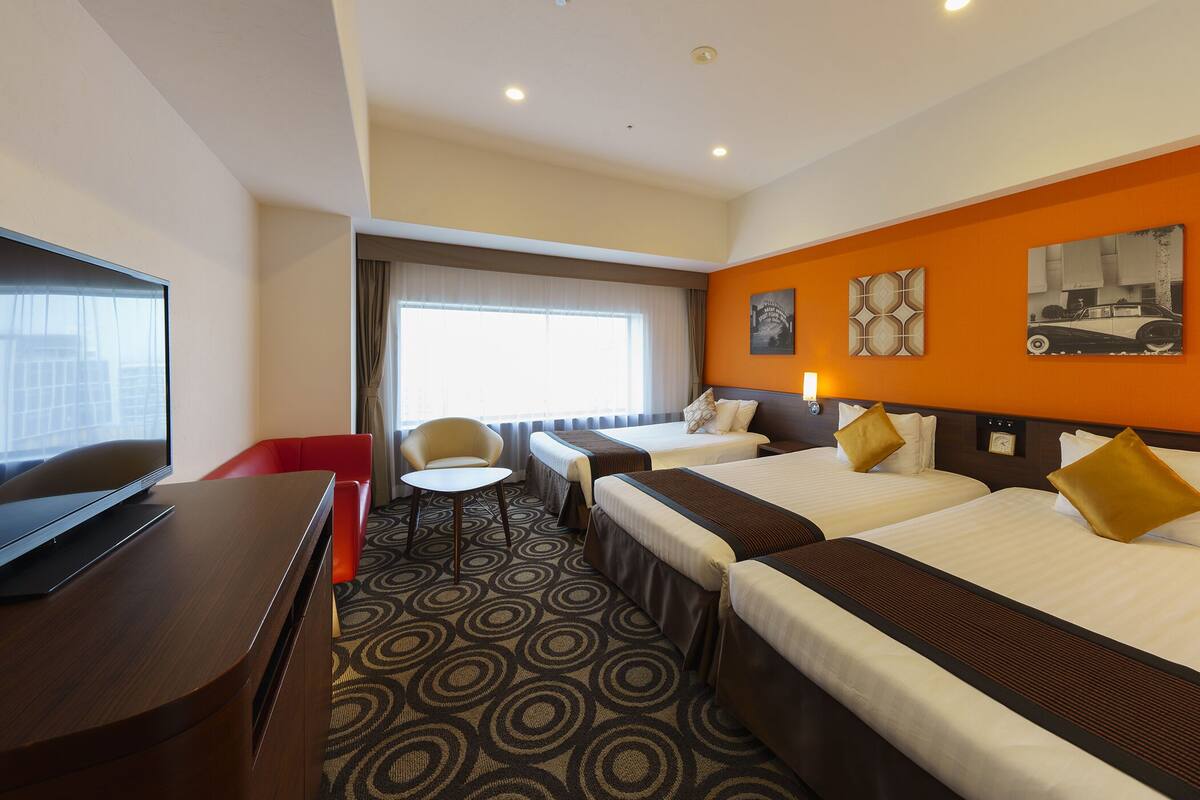 Een hotelkamer met twee bedden, een televisie, een bureau en een raam met gordijnen.