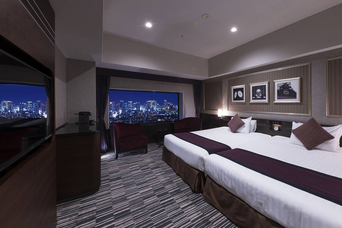 Quarto de hotel com vista para a cidade, uma cama grande, uma escrivaninha e uma televisão.