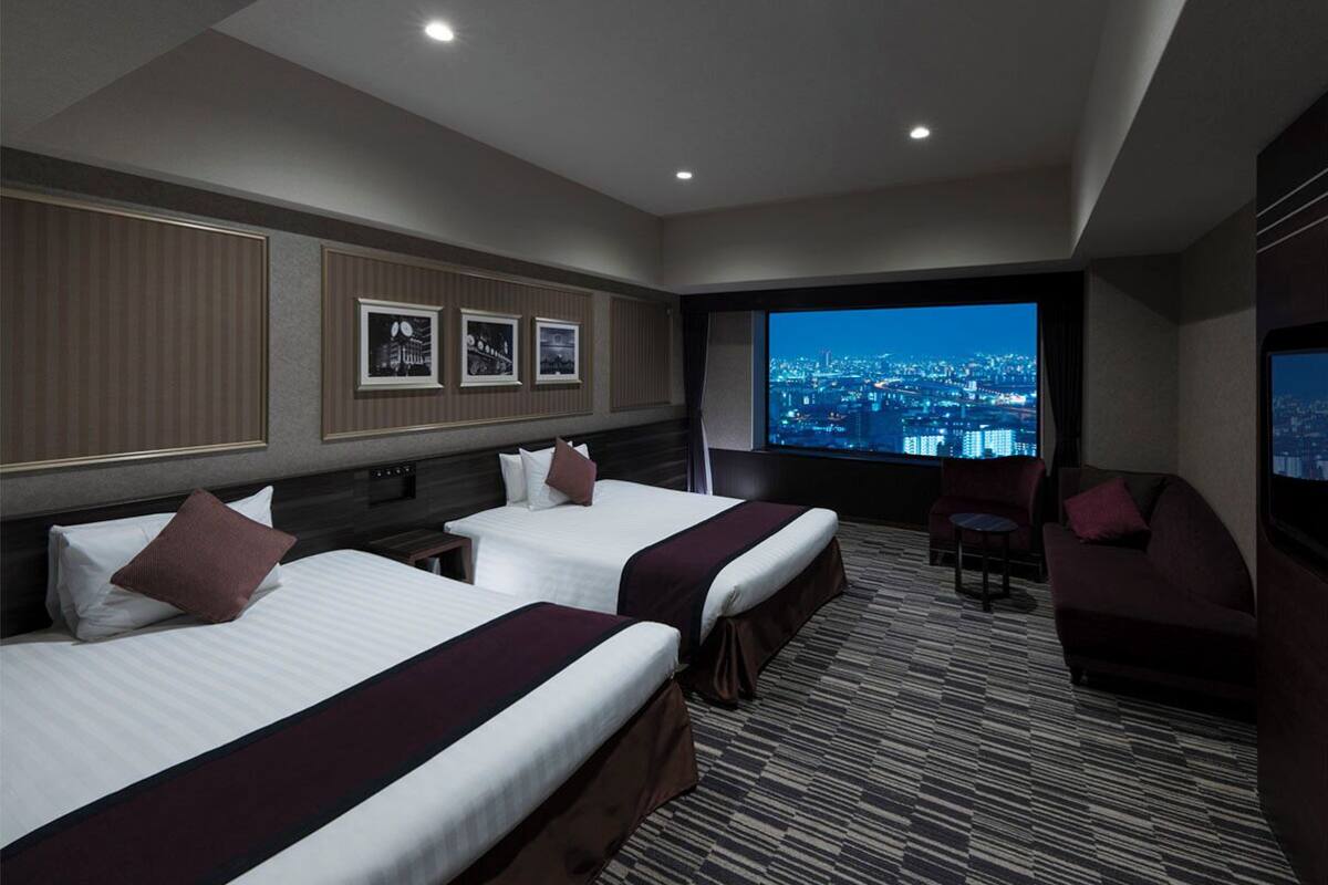 Quarto de hotel com duas camas, um sofá, uma TV e vista para a cidade.