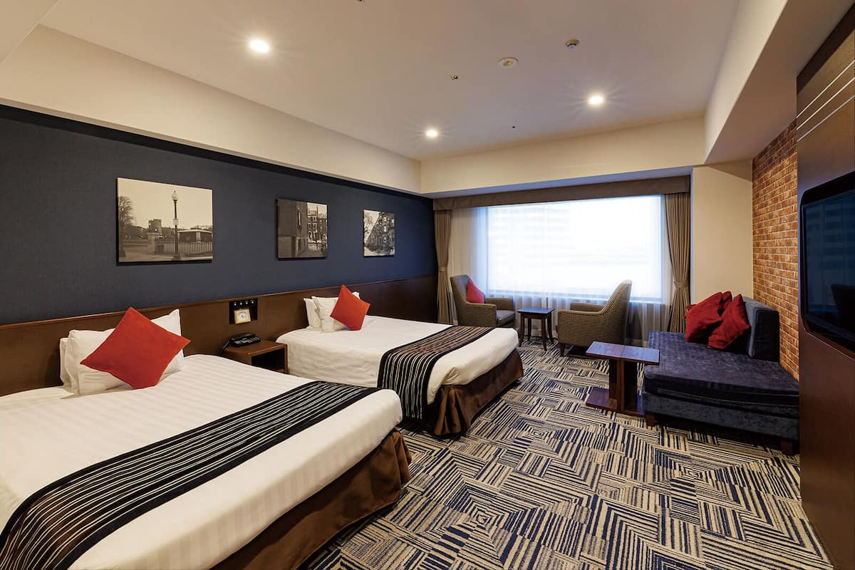 Een hotelkamer met twee bedden, een bank, een televisie en een raam met gordijnen.