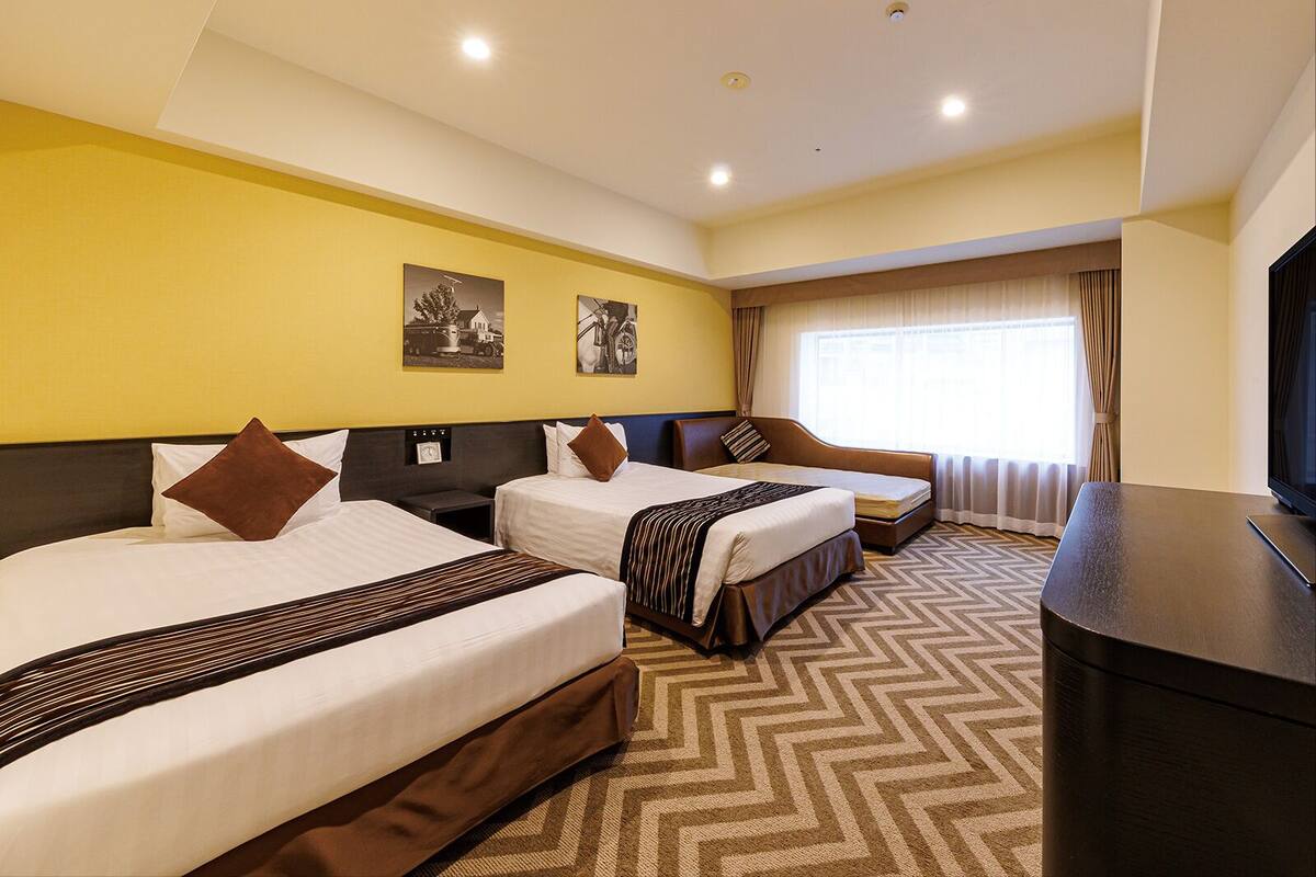 Een hotelkamer met twee bedden, een televisie en een raam met gordijnen.