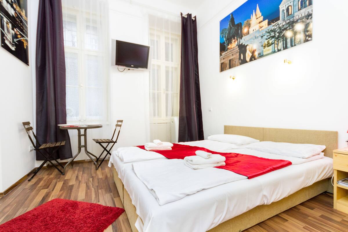 A hotel room with a bed, a desk, a chair, a TV, and a painting on the wall.