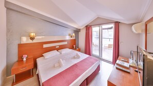 Habitación de hotel con una cama grande, una mesita de noche con lámpara, un escritorio con televisor y un ventanal corredero al exterior.