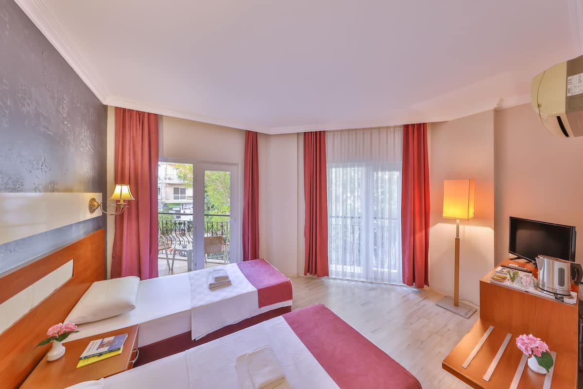 A hotel room with two beds, a TV, a desk, and a balcony with red curtains.
