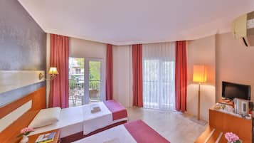Habitación de hotel con dos camas, televisión, escritorio y balcón con cortinas rojas.
