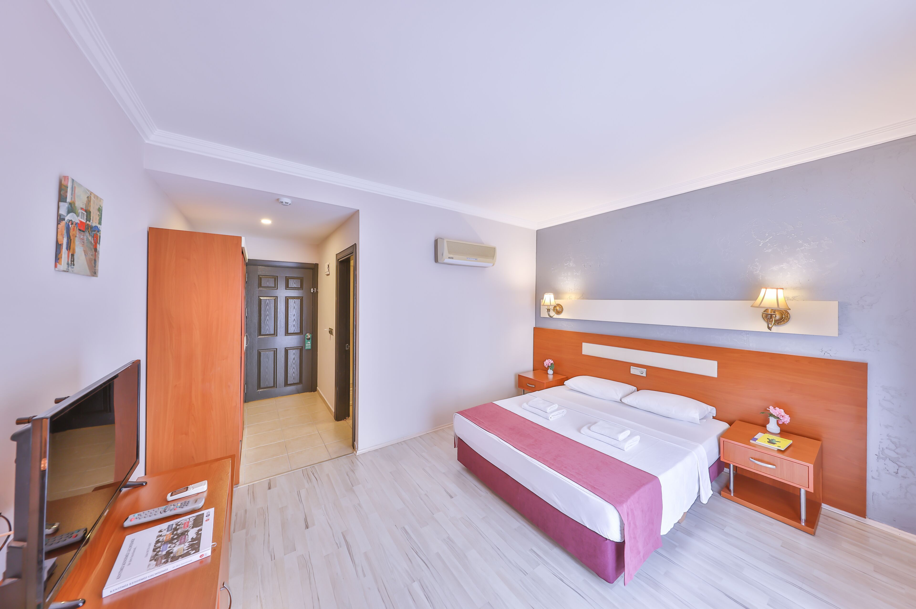 A hotel room with a bed, bedside tables, a TV, and a door leading to another room.