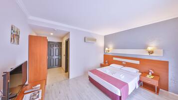A hotel room with a bed, bedside tables, a TV, and a door leading to another room.
