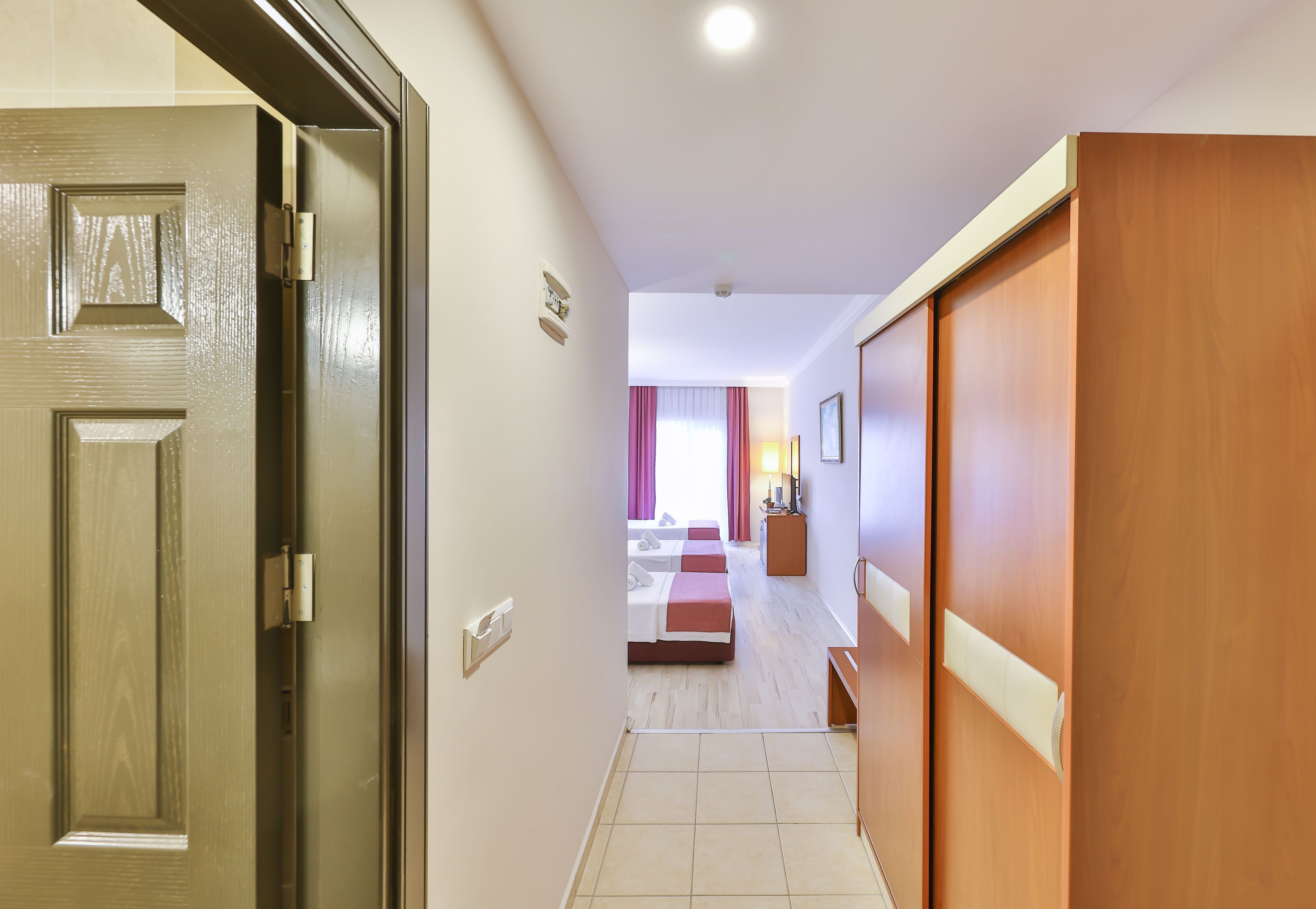 A hotel hallway with a wooden door, a bed, a nightstand, and a lamp.
