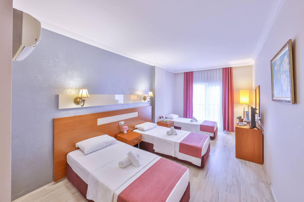 A hotel room with three beds, a desk, a chair, a TV, and a window with curtains.
