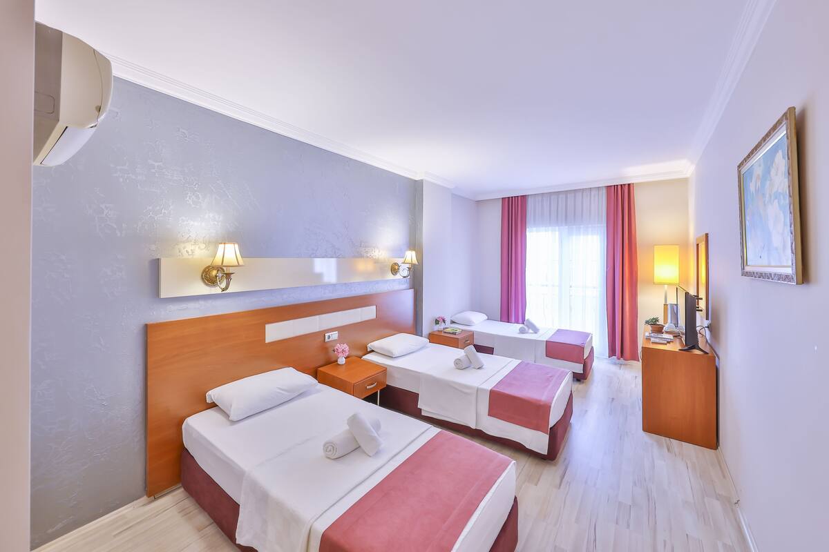 A hotel room with three beds, a desk, a chair, and a window with curtains.
