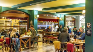 Un interior de restaurante con mesas y sillas de madera, una barra con menú y una vitrina de vidrio.