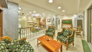 Uma sala de estar ampla com uma mesa de centro de madeira, dois sofás com padrão verde e uma poltrona de madeira.