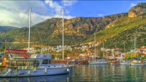 Un puerto deportivo con barcos amarrados, un telón de montañas al fondo y un pueblo costero con edificios.