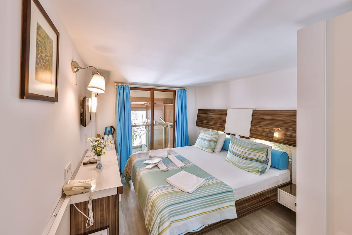 Hotellihuone, jossa on sänky, yöpöytä, lamppu ja lasiovesta avautuva näkymä.