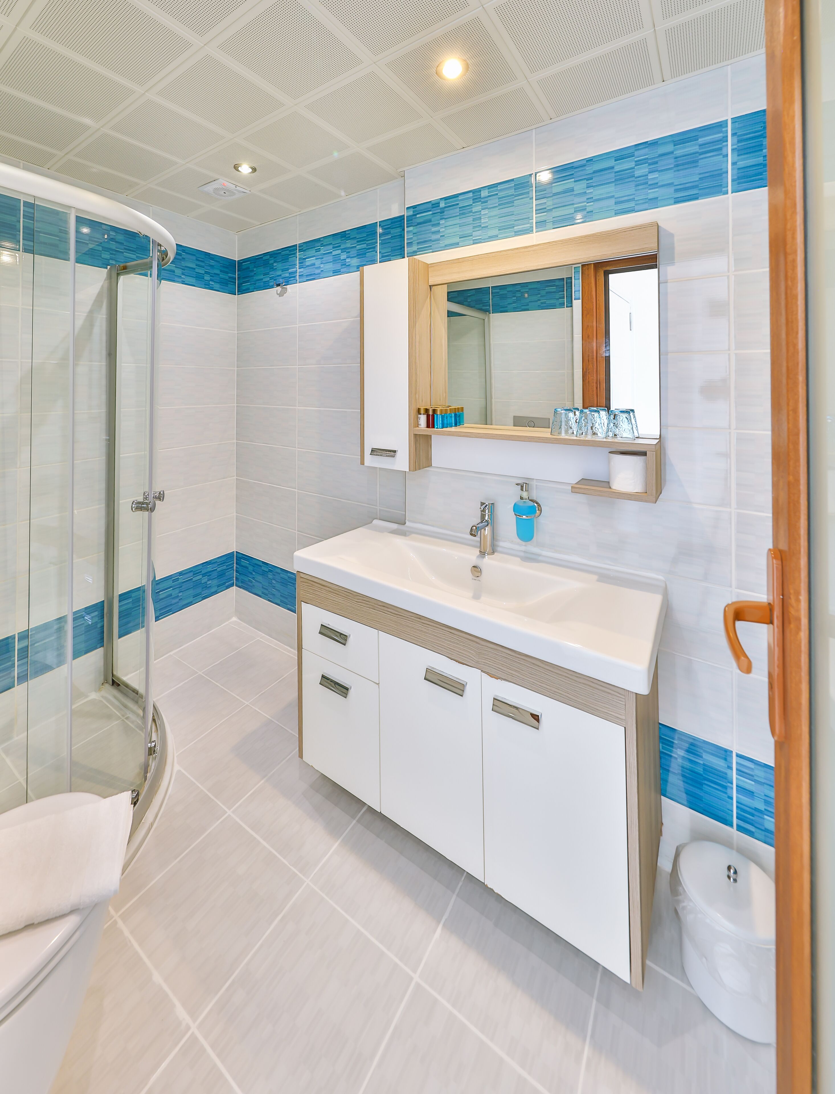 Un baño moderno con cabina de ducha de vidrio, un lavamanos blanco con encimera de madera y un espejo sobre el lavamanos.