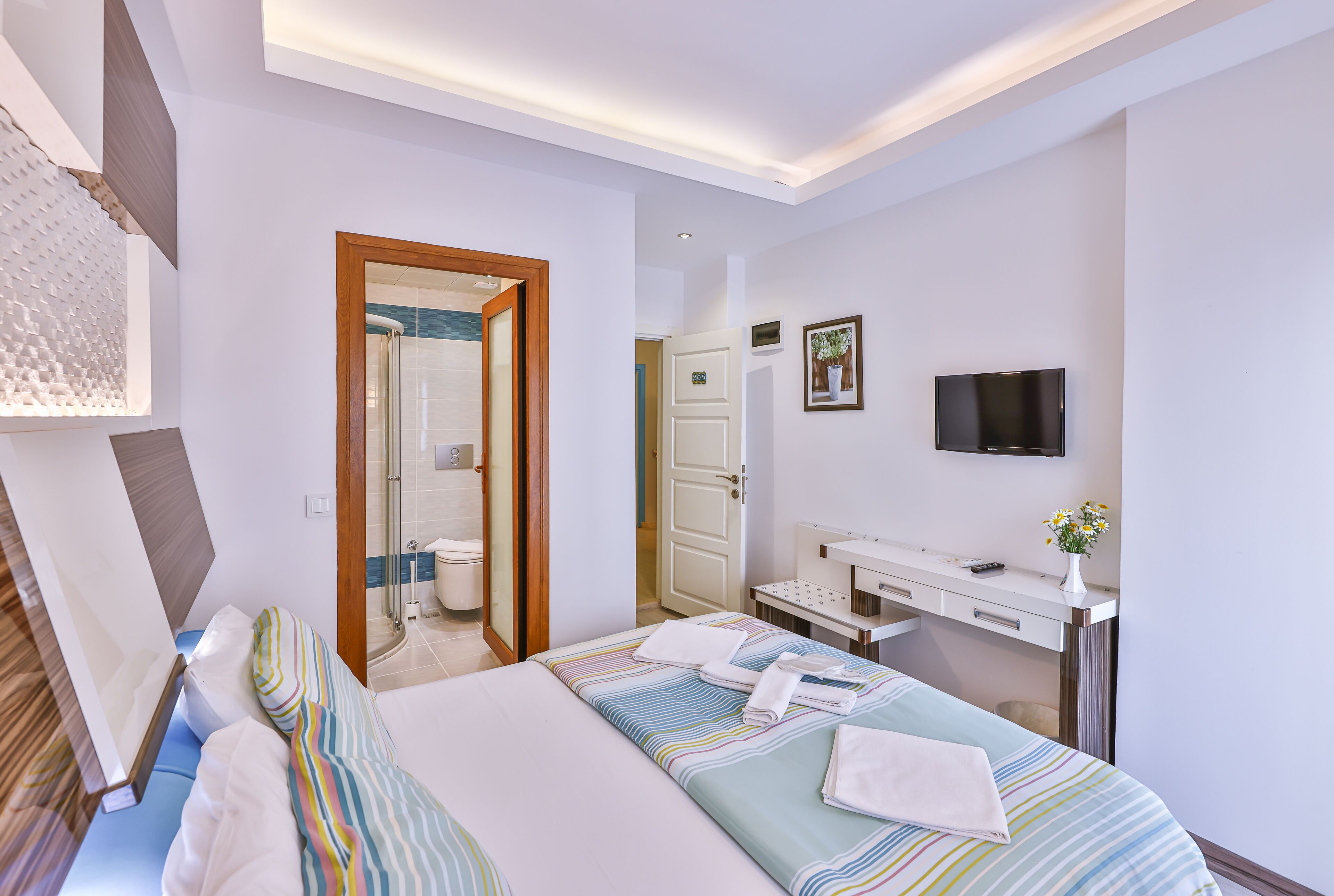 A hotel room with a bed, bedside table, TV, and a bathroom visible through an open door.