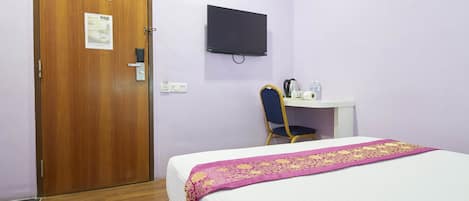 Habitación de hotel con puerta de madera, cama con edredón blanco y rosa, escritorio con silla y televisor montado.