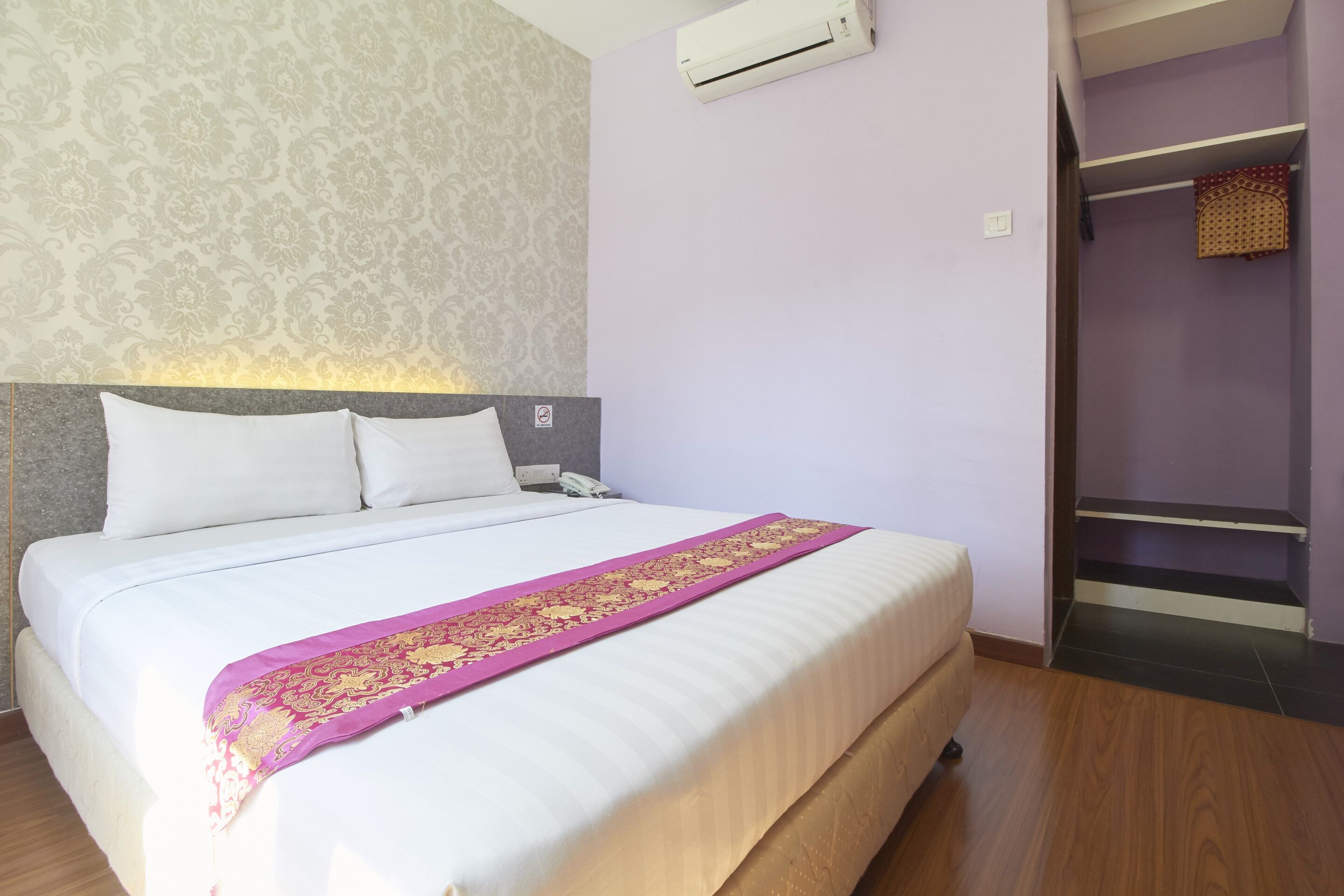 Habitación de hotel con cama, cabecera, aire acondicionado, armario y papel tapiz estampado.