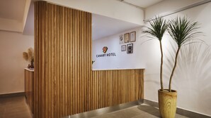 A reception desk with vertical wooden slats, a potted plant, and a wall displaying the Canary Hotel logo and framed certificates. - Canary Hotel (Kuala Lumpur)