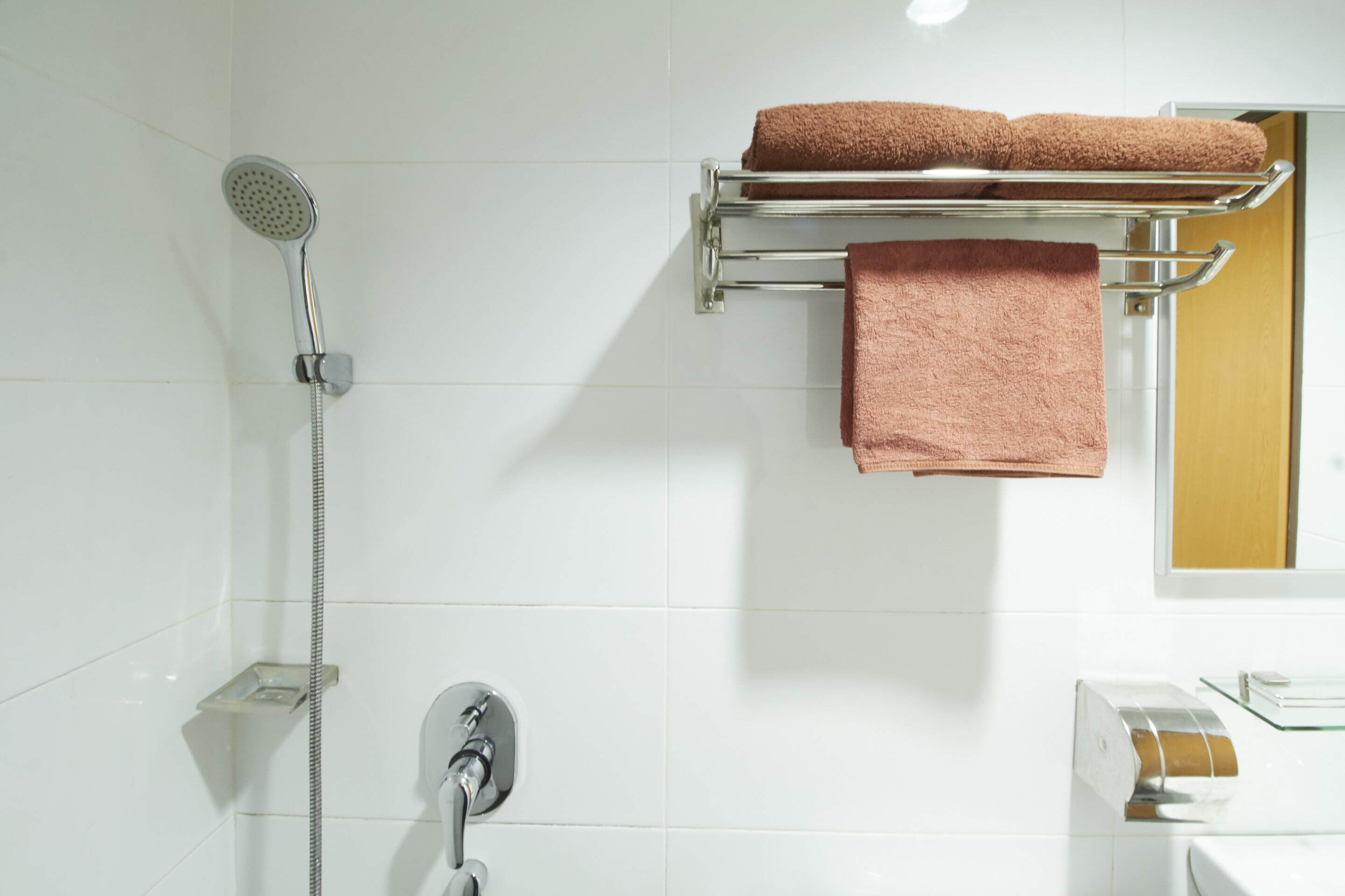 Une salle de bain avec une douche, un porte-serviettes avec deux serviettes, un savonnière en verre et des toilettes.
